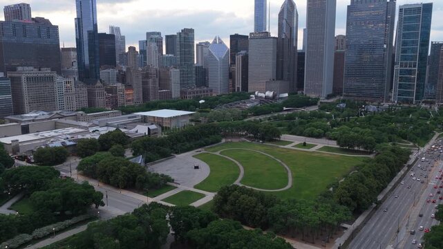 Pull up aerial establishing shot of downtown Chicago's impressive skyline, skyscrapers towering over Maggie Daley Park and city streets filled with early evening traffic