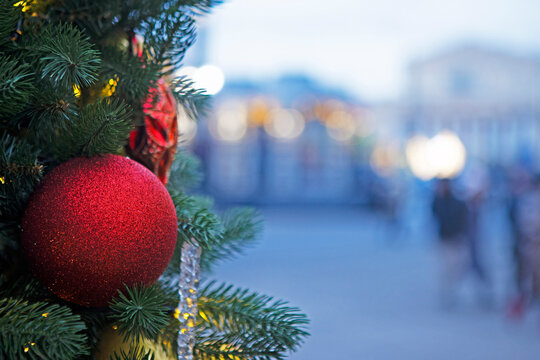 Red ball on Christmas tree on background of city street. Street is out of focus. Background for Christmas card. Place for advertising