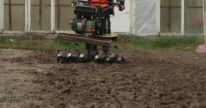 Gardener using a motor-cultivator to plow the soil in a small garden plot, preparing the fertile ground for planting crops and making the soil looser for the upcoming growing season