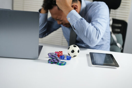 A young man loses a bet while gambling on soccer, facing failure and regret. He displays a depressed expression in front of his laptop, playing soccer and losing all his money, losing his gambling.
