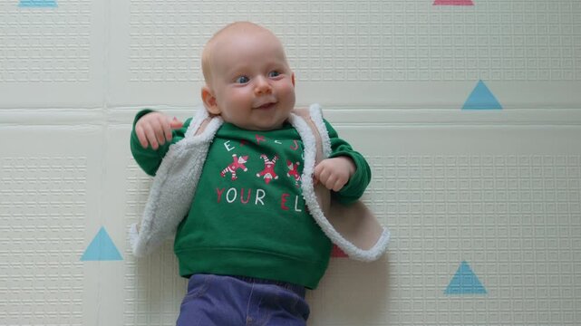 Smiling three month old baby in christmas outfit on floor rug. Slow motion.