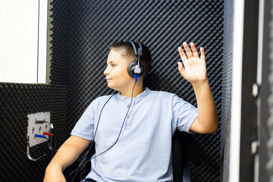 A child undergoes a hearing test in a soundproof booth wearing headphones. The child raises their hand because they have heard a ringing sound. Concept of hearing prevention in children.