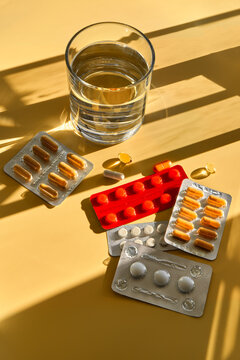 Medications and dietary supplements with glass of water in sunlight.