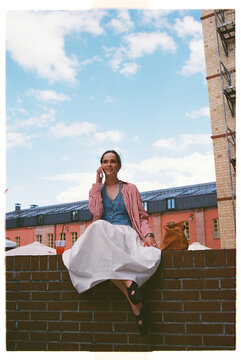 Woman sits on a brick wall while talking on the phone