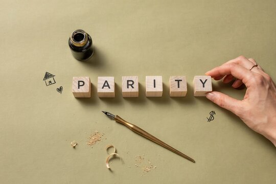 A hand arranging wooden blocks spelling parity with scattered letters and an inkwell on a table
