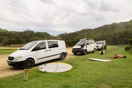 Surfer stretching beside campervans and surfboard in NSW national park