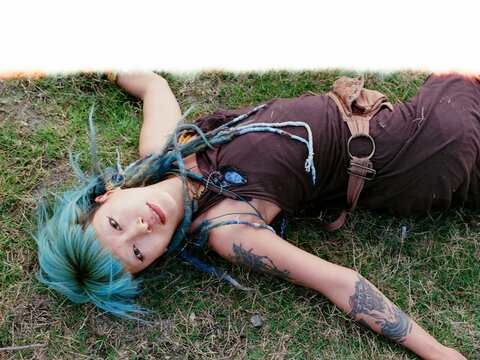 Young Woman with Blue Hair and Tattoos Lying on Grass