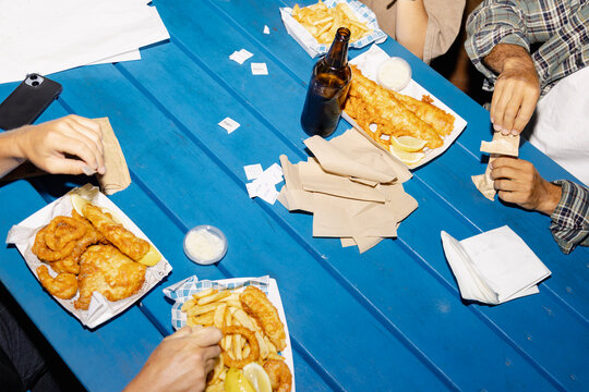 Anonymous friends sharing fish and chips on blue picnic table