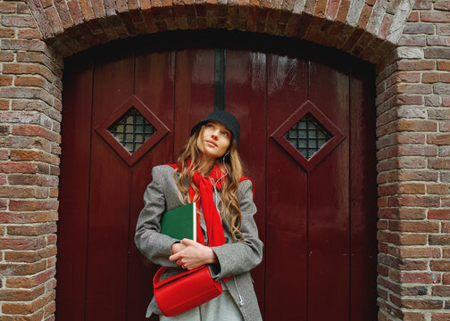 Young Woman Stands at Red Brick Wall With Bag and Notebook