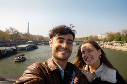 Cheerful couple taking a selfie by the Seine River in Paris
