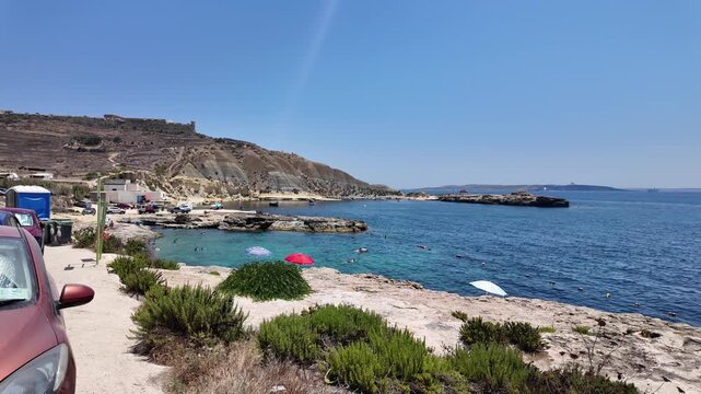Mgarr, Gozo - 29.06.2026 - Xatt L-Ahmar, salt pans view towards cliffs from the parking stationary beach scene with car and hills 