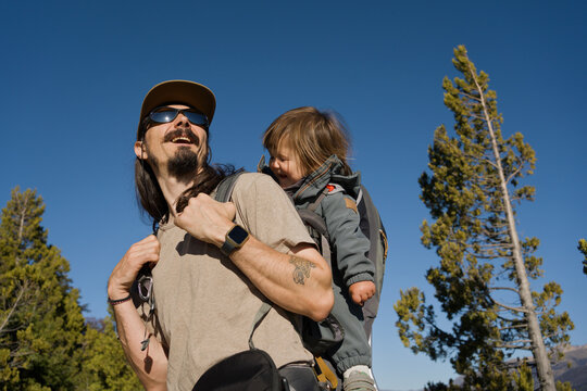 Father Carries Child on Back During Hike in Woods