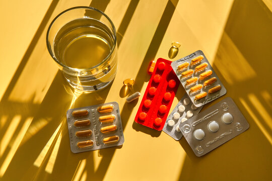 Medications and dietary supplements with glass of water in sunlight.