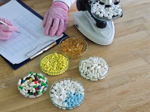 Laboratory worker examines medications and supplements with microscope on workspace
