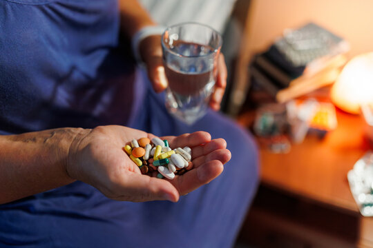 Close up of human hands holding medication pills and clear water glass.