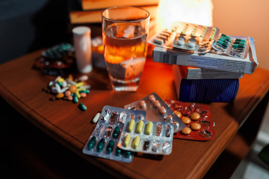 Medicine tablets and clear water glass resting on nightstand in dark room.