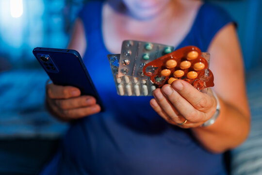 Senior lady wearing glasses examining medical pills in dark bedroom at night.