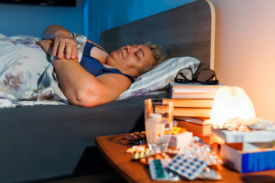Senior woman sleeping in dark bedroom near medical pills at night.