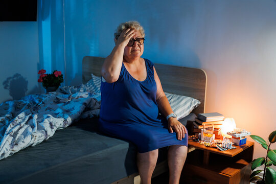 Mature woman massaging head suffering intense headache in dark bedroom.