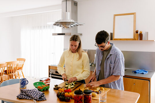 A couple stands at a kitchen island, slicing fresh vegetables.