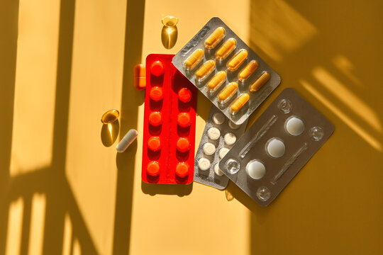 Medications and dietary supplements on yellow background in sunlight.
