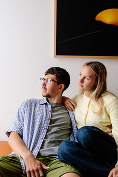 A man with glasses and a blonde woman sit closely together indoors.