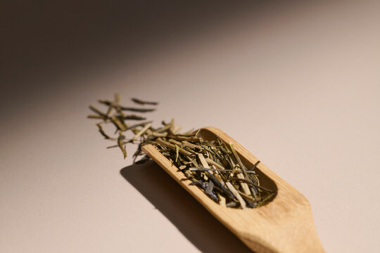 Dried green tea leaves in a wooden scoop with dramatic lighting