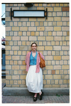 Woman stands against a brick wall wearing a striped jacket
