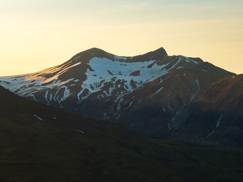 Aerial view of Thorsmork mountain range with snow-capped peaks illuminated by the soft golden light of the setting sun in Rangarthing eystra, Iceland.