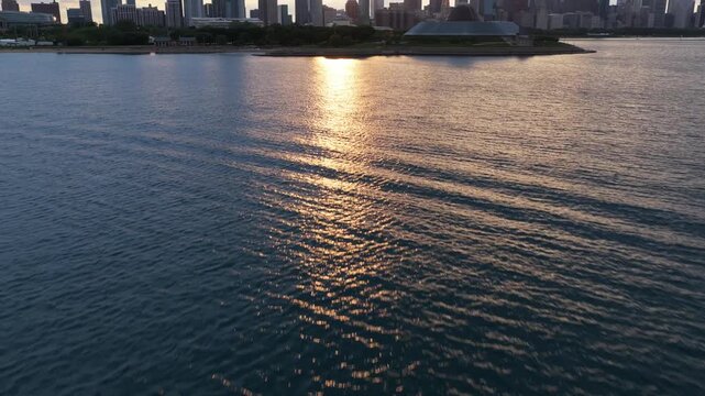 Aerial tilt up of motorboat sailing on Lake Michigan with Chicago skyline during sunset, Shedd Aquarium, Willis Tower, sun glitter and water ripples