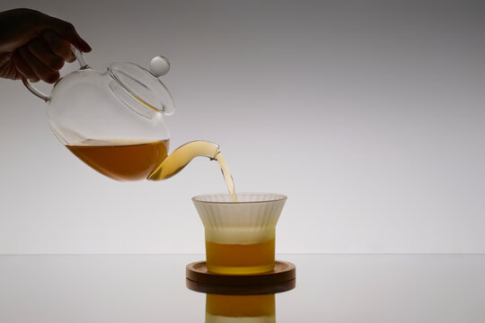 Pouring amber liquid from a glass teapot into a frosted glass