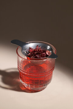 Steeping dried hibiscus flowers in a glass of vibrant red herbal tea