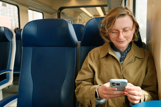 Happy smiling woman on a train holding her smartphone while texting 