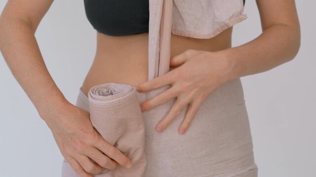 Postpartum belly binding with long fabric wrap. Close-up. Slow motion.