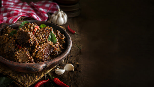 Traditional beef rendang slow cooked spicy meat dish in clay pot with rustic textures.