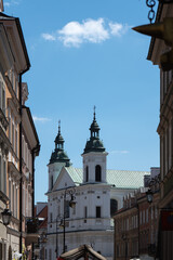 Fototapeta premium Historic church towers stand at old town street city landmark. Ancient European architecture building facade represents Poland history heritage site tourism and summer travel destination.