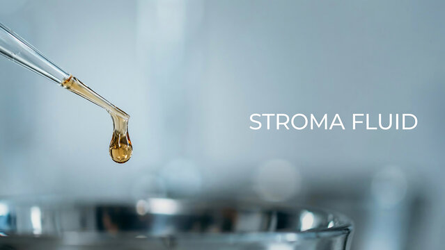 A single drop of amber colored stroma fluid hanging from a glass pipette tip over a laboratory glass container