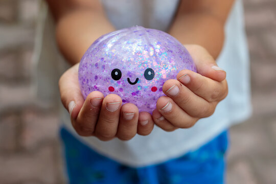 Smiling little boy playing with a glittery dumpling shaped squishy toy outdoors, squeezing a colorful sensory stress relief toy during fun playtime in the garden