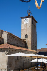 Obraz premium Romanesque Santiago church facade and traditional gallery building at Praza Maior in Allariz, Ourense, Galicia, Spain. Tourists walking by ancient stone architecture under a summer blue sky.