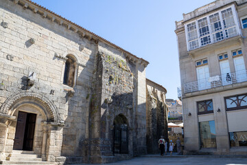 Fototapeta premium Romanesque Santiago church facade and traditional gallery building at Praza Maior in Allariz, Ourense, Galicia, Spain. Tourists walking by ancient stone architecture under a summer blue sky.