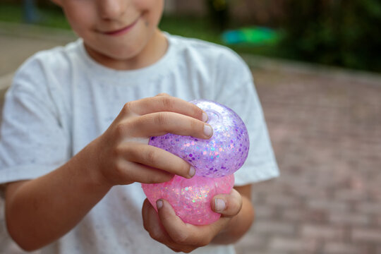Smiling little boy playing with a glittery dumpling shaped squishy toy outdoors, squeezing a colorful sensory stress relief toy during fun playtime in the garden