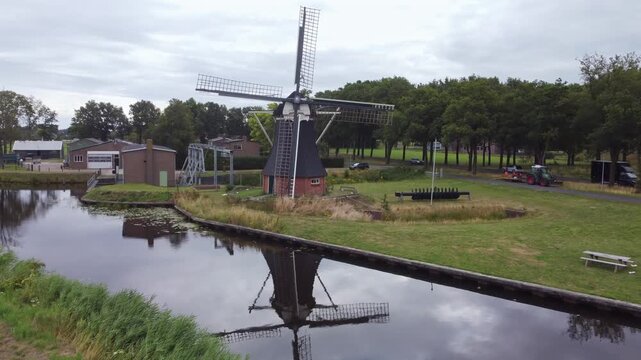 Historic De Boezemvriend drainage windmill in De Groeve, Netherlands, with its reflection on the water of the canal on a cloudy day