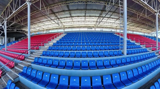 Covered stadium grandstand with red and blue seats captured in smooth moving 4K video
