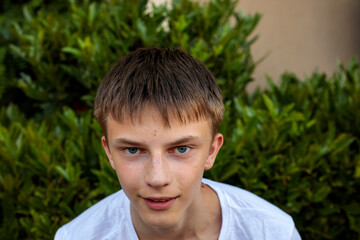 A close up portrait shows a teenage boy with striking blue eyes and freckles against a green garden backdrop, capturing a range of natural facial expressions © Татьяна Швец
