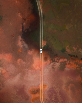 Aerial view of a car driving along a dirt road through a vast red volcanic landscape in Iceland.