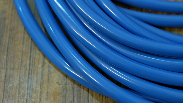 A high-angle, close-up shot capturing a neatly coiled bundle of thick, glossy blue plastic tubing or cable resting on a textured wooden surface.