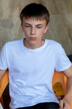 A close up portrait shows a teenage boy with striking blue eyes and freckles against a green garden backdrop, capturing a range of natural facial expressions