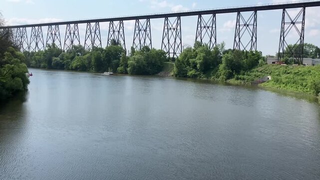 Unrecognizable people in pontoon and pedal boats moving up the Cap-Rouge river in summer, with the 1908 railway trestle bridge in the background, Quebec City, Qu&eacute;bec, Canada