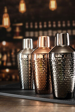 Three shakers of different colors stand against background of bar. Shakers are made of copper, steel and ferrous metals. Shakers stand on rubber mat. Classic accessories for bartender