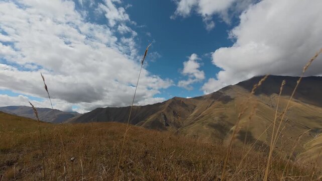 4K timelapse video of white clouds moving over beautiful golden grass field and rolling mountain range.